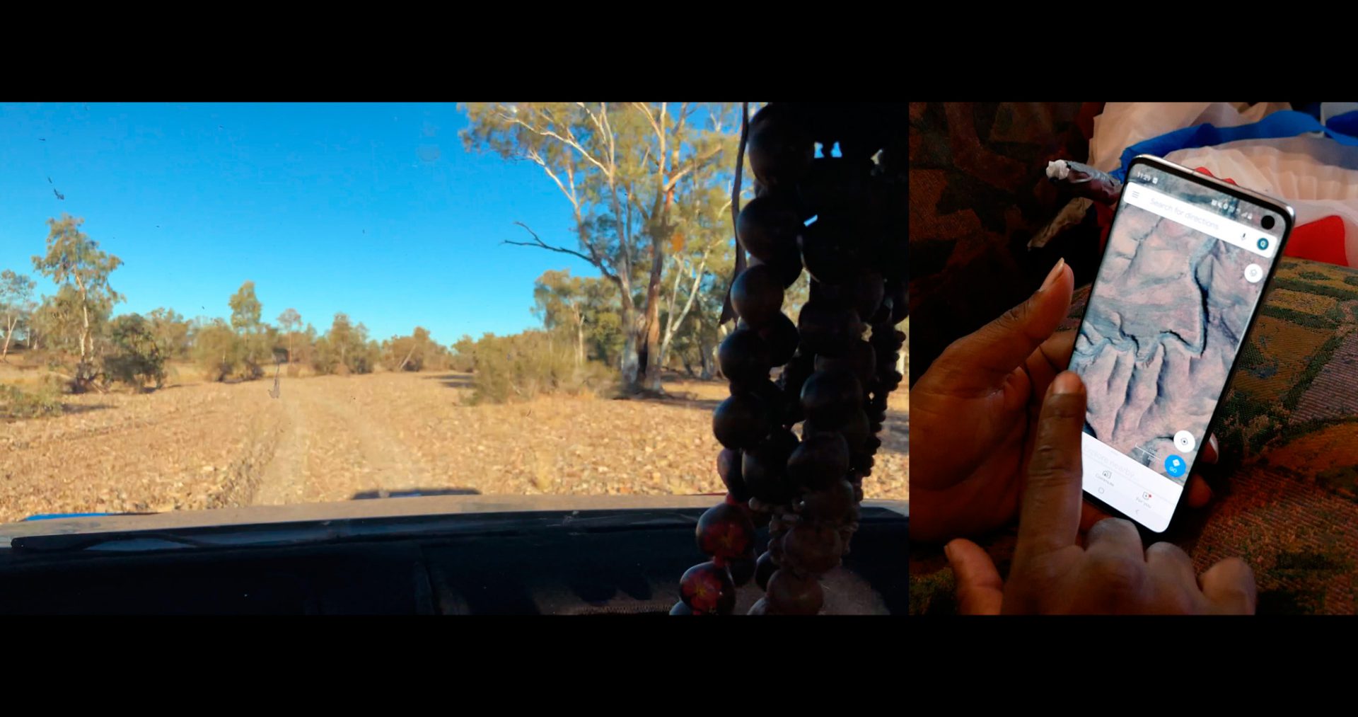 A horizontal image and a vertical image are laid out together. On the left, the horizontal image depicts an arid desert landscape from the perspective of a car dash. In the foreground, chunky beads hang from the rearview mirror. In the background are dry mud flats, scrub trees and bushes, and cloudless blue sky. On the right portrait-oriented image, a brown-skinned left hand holds out a smartphone and the right-hand index finger points at an image on the smartphone screen. The smartphone screen depicts a topographical satellite image of a dry landscape with a water-less river bed.